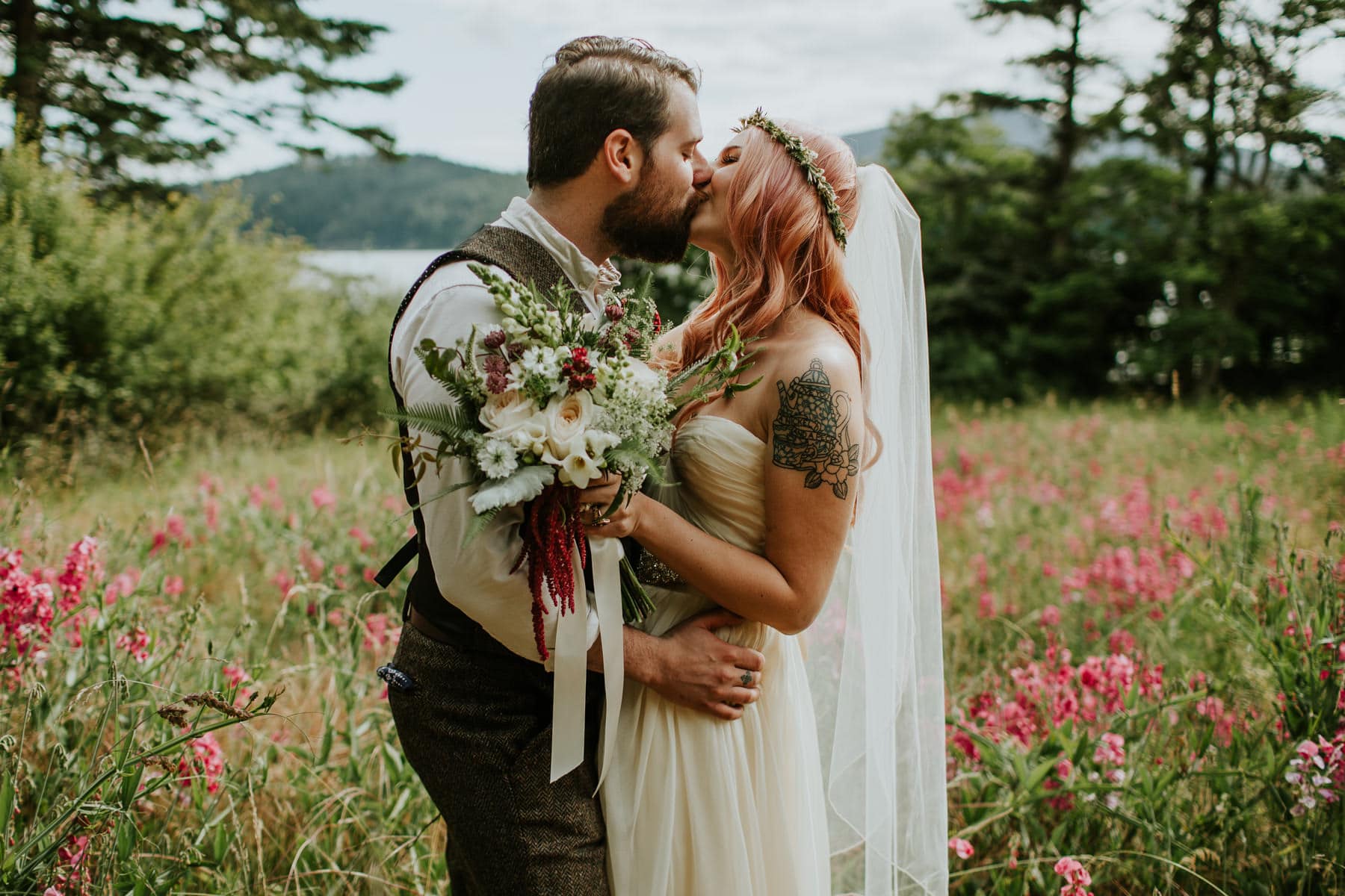 groom kissing bride with pink hair flower field